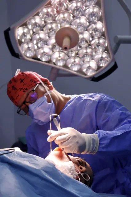 Chirurgien concentré sur son geste opératoire, loupes chirurgicales et éclairage de bloc